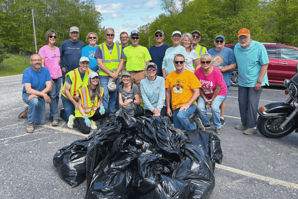 Group of community members at community clean up, wearing colorful shirts with garbage bags displayed in front